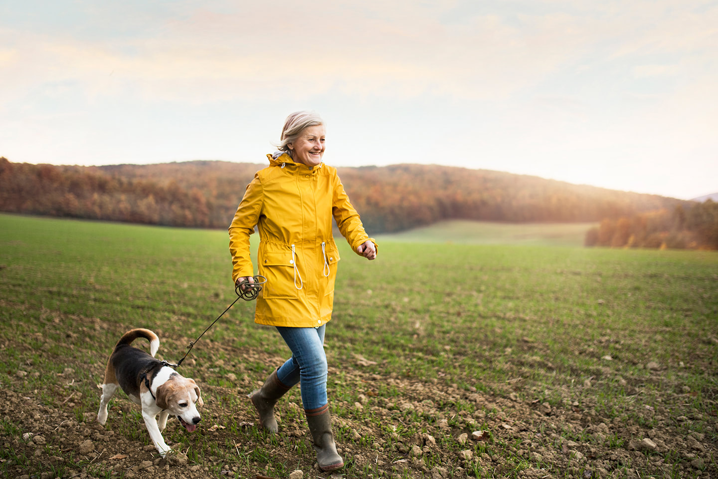 Seniorka v žlutém kabátu se psem procházce na poli